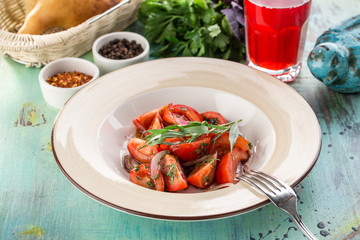 healthy appetizer fresh tomato salad in white bowl with red onion and estragon on blue wooden table