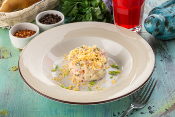 Russian traditional salad Olivier with egg yolk and glass of red drink on blue wooden table