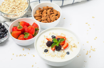Greek yogurt with granola fresh strawberries, blueberries, blackberries and almonds on white table. Healthy snack. Breakfast food. 