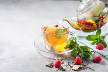 Pouring tfrom a teapot into a cup hot herbal tea with lemon, raspberries and mint. Healthy lemon tea.