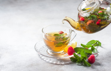 Pouring tfrom a teapot into a cup hot herbal tea with lemon, raspberries and mint. Healthy lemon tea.
