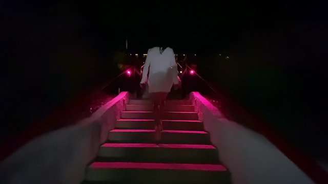 Female walking up a flight of step outside at night.  Pink glow of light on stairs
