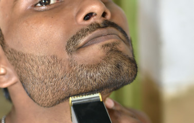 A closeup of a young man trimming his beard with an electric trimmer