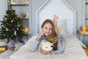 A little girl with blonde hair plays with her stuffed toy, waits and looks at Christmas gifts in the children's playroom