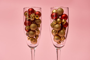 Champagne glasses with golden and red baubles on pastel pink background, copy space. Minimal, New year concept