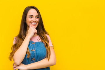 young pretty woman smiling with a happy, confident expression with hand on chin, wondering and...