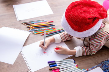 A beautiful girl with christmas hat using color pencil writing on paper in classroom. Exams at the...