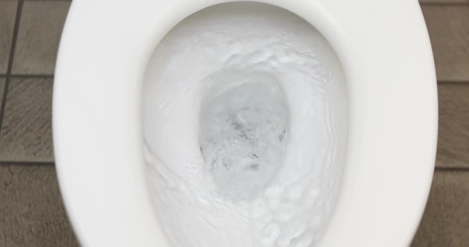 From above clean water flushing in white toilet in public water closet close up