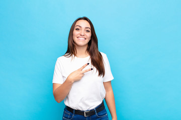 young pretty woman feeling happy, positive and successful, with hand making v shape over chest,...