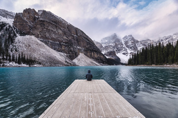 Traveler sitting on wooden pier with rocky mountain in Moraine lake at Banff national park
