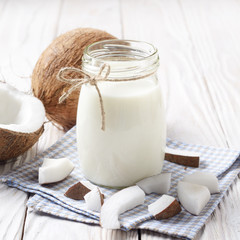 Mason jar of milk or yogurt on blue napkin on white wooden table with coconut aside