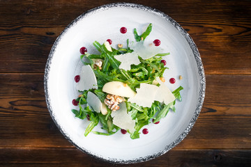 Fresh Salad with arugula, Parmesan cheese, potatoes and nuts on a white plate on wooden background