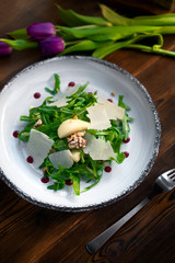 Fresh Salad with arugula, Parmesan cheese, potatoes and nuts on a white plate.