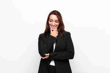 young pretty businesswoman smiling with a happy, confident expression with hand on chin, wondering...