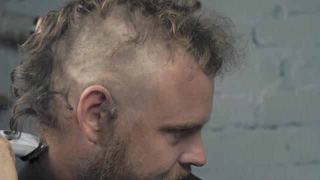 a man with a beard shaves his head with an electric trimmer. bearded punk hipster shaves his mohawk. 4k video. 59.94 fps