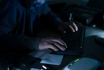 Closeup of hacker`s hands on the desk keyboard, different devices on the table at the...