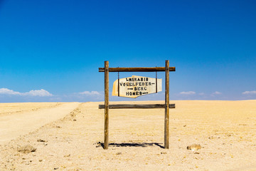Old wooden sign next to a gravel road, vast desert, Namibia, Africa