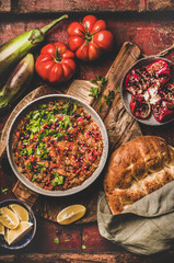 Turkish and Middle East traditional meze starter. Flat-lay of Babaganoush cold dip seasoned with parsley and pomegranate seeds with flatbread over rustic background, top view. Oriental typical salad