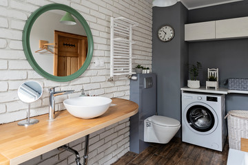 Interior of bathroom with white brick wall, modern washbasin and wooden countertop. Industrial...