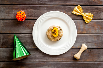 Birthday party for puppy concept. Dog feed, candle, bone, party hat on dark wooden background top-down