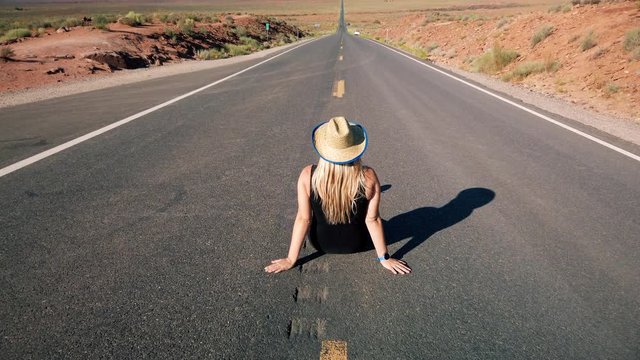 Young blonde girl sits in the center of Forrest Gump Point Road to Monument Valley, region of Colorado Plateau buttes Arizona&ndash;Utah border. Slow motion Gimbal panning cinematic Rec.709 ProRes 422