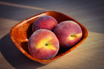 wooden bowl with three ripe peaches