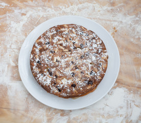 Round cake with almonds on a white plate lies on a cutting Board with flour.