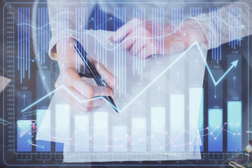 Hand taking notes in notepad. Forex chart holograms in front. Concept of research. Multi exposure