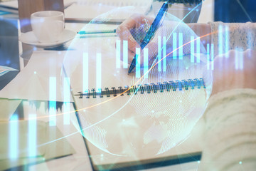 Forex chart hologram on hand taking notes background. Concept of analysis. Double exposure