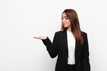 young pretty businesswoman feeling happy and smiling casually, looking to an object or concept held...