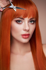 Beautiful young woman with a bright makeup and a smooth long hair holds metal scissors. Model with...