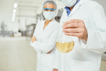 Worker in masks and coats look at the liquid in the flask at work.