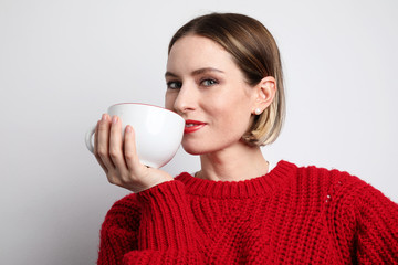 Young woman wearing casual clothing and drinking hot coffee. Isolated.