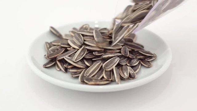 Sunflower grains spilling on a rotating plate on a white background
