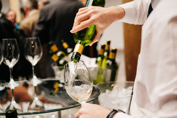 A waiter pours wine from a bottle into a glass at an event, meeting, wedding or congress