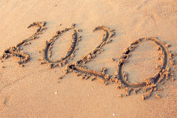 020 text painted on the yellow sand on the beach.