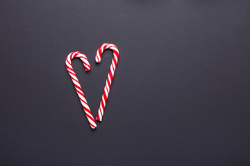 Two candy canes in shape of heart on black wooden background. Christmas, winter, new year concept -...