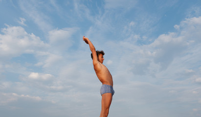 athletic teenager on the beach in swimming trunks against the sky