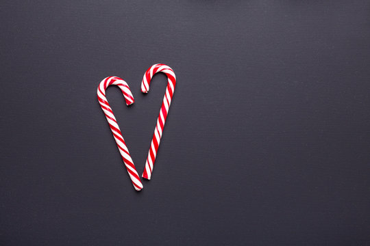 Two candy canes in shape of heart on black wooden background. Christmas, winter, new year concept - Image
