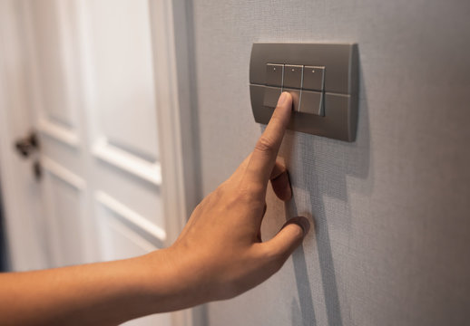 Asian female left hand is turning off on grey light switch.