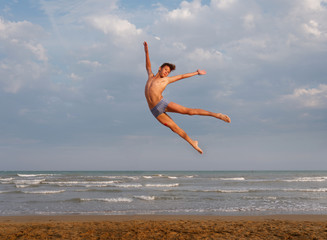 athletic teenager on the beach in jump on the background of the sea and sky