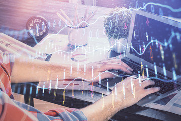 Double exposure of stock graph with businessman typing on computer in office on background. Concept of hard work.