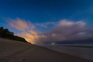 Gewitter und Sterne über dem Strand am Meer bei Nacht