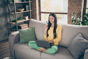 Full length photo of positive cheerful girl sit divan legs crossed use computer want buy new dress use plastic card easy payment concept in house indoors