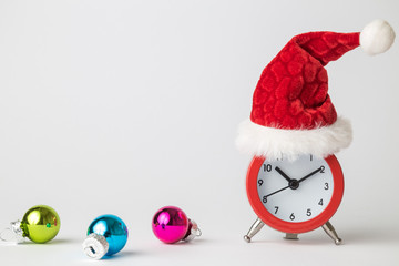 Small analog clock with Santa Claus hat and multicolored baubles abstract isolated on white. Winter season and christmas time concept.