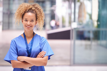 Portrait Of Female Doctor Wearing Scrubs Standing In Modern Hospital Building