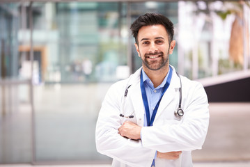 Porträt eines männlichen Arztes mit Stethoskop im weißen Kittel, der im modernen Krankenhausgebäude steht