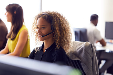 Young Businesswoman Wearing Telephone Headset Talking To Caller In Customer Services Department