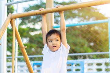Obraz premium Kid exercise for health and sport concept. Happy Asian child boy playing and hanging from a steel bar at the playground. 5 years old.