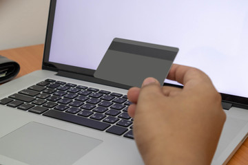 A man hand holding a credit card using a laptop to shopping online. Soft focus of young man of working using a laptop, Business concept, and communication technology. white blank screen